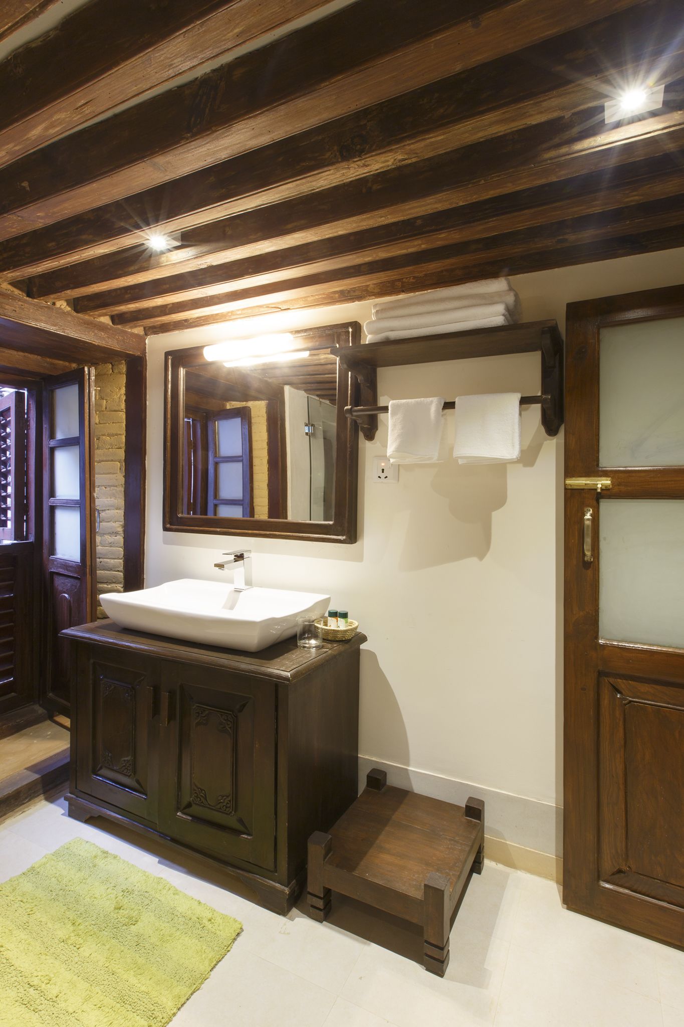 A bathroom with a wooden vanity, a white sink, a mirror, and a towel rack.