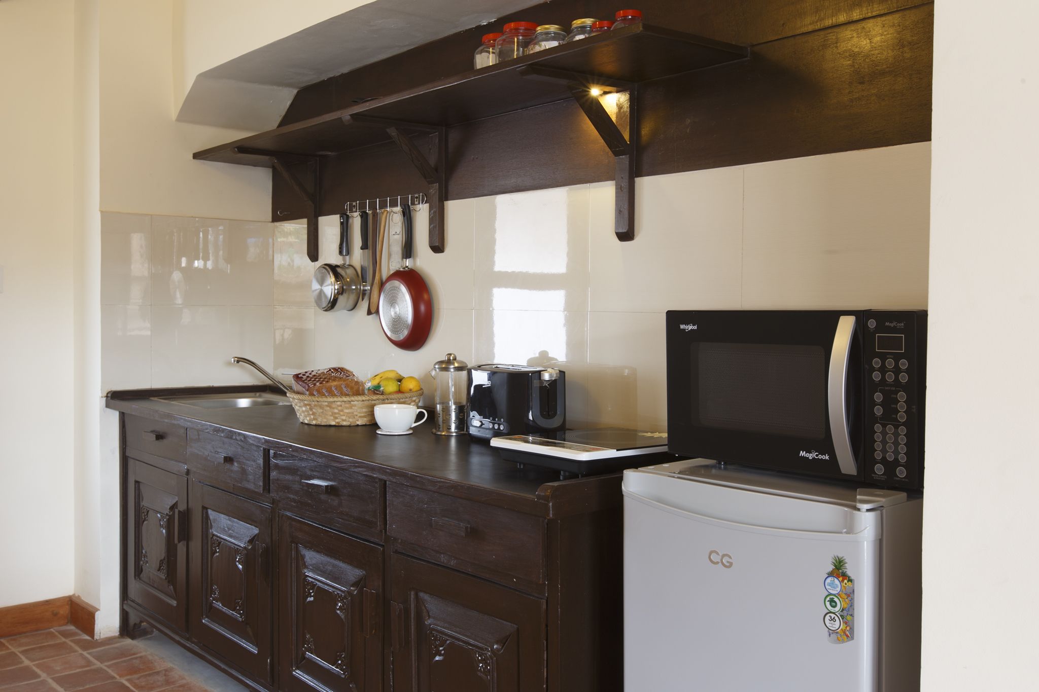 A kitchen with dark wooden cabinets, a white refrigerator, a microwave, a toaster, and hanging utensils.