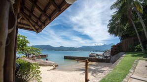 A beach view with a wooden deck, a stone pathway, and a palm tree.