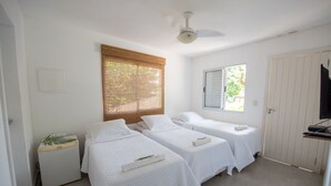 A room with two single beds, a small refrigerator, a ceiling fan, a window with blinds, and a door.