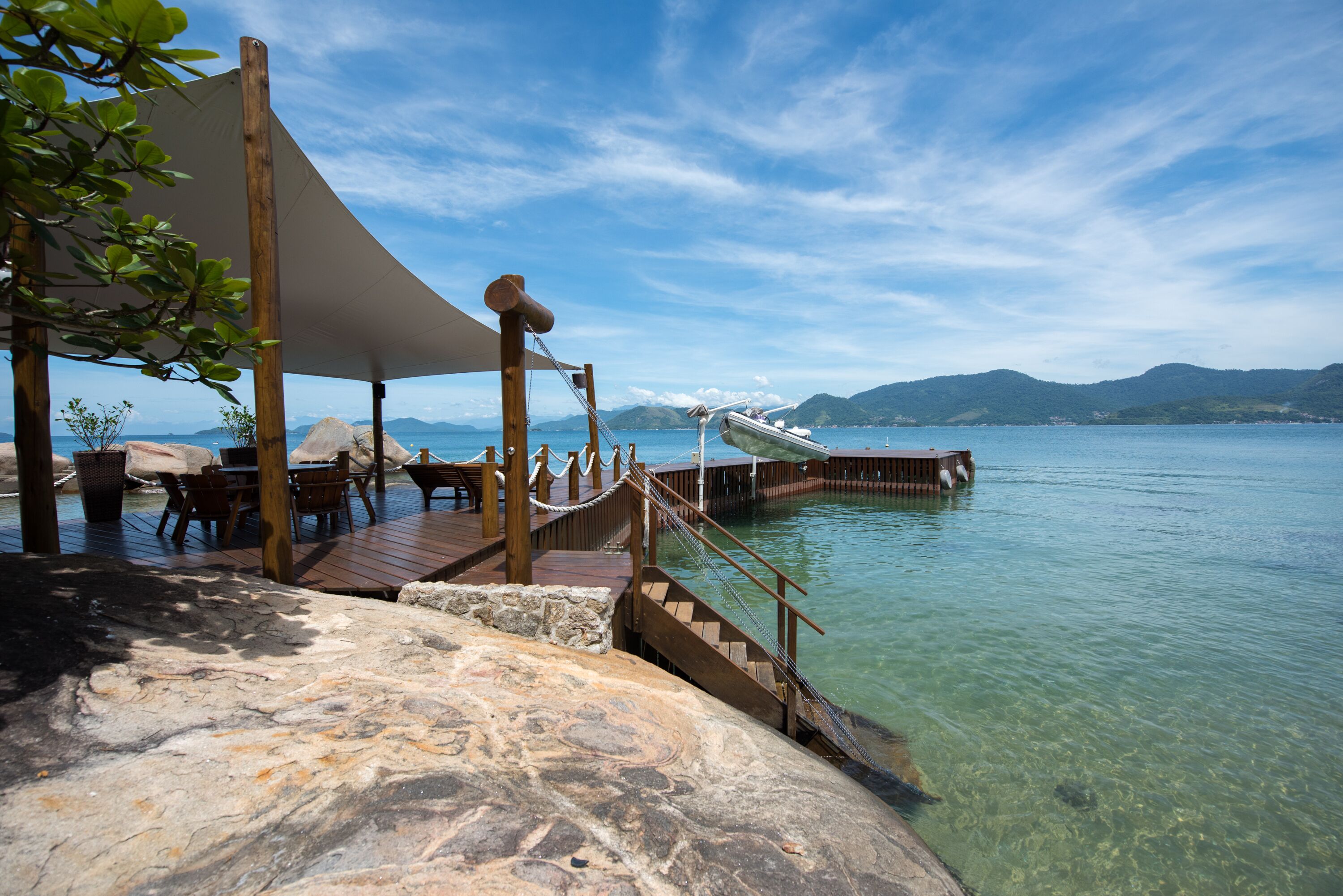 Ein Holzdeck mit Seilsicherung, klarem Wasser und fernen Bergen.