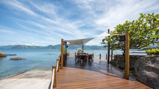 A wooden deck leading to a table and chairs by the water, with a rope barrier and a canopy.