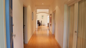 A hallway with wooden flooring, a staircase, and a dining area in the background.