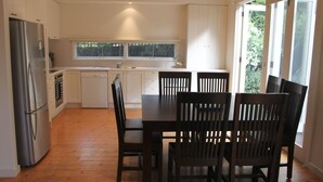 A modern kitchen with white cabinetry, a stainless steel refrigerator, a dishwasher, and a dining area with a dark wooden table and chairs.