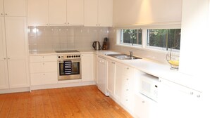 A modern kitchen with white cabinetry, a stainless steel oven, a sink, and a window overlooking a green area.