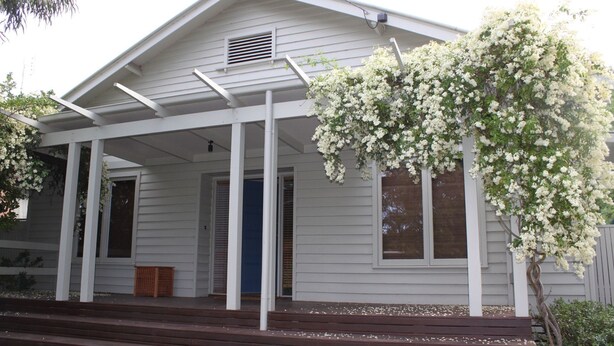 A white house with a covered porch and a flowering tree.