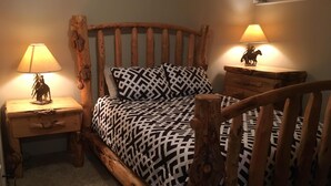 A rustic wooden bed with a geometric patterned bedspread, flanked by two nightstands with lamps and a small statue. - Cozy Cabin In Twin Falls (Twin Falls)
