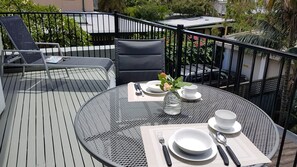 Een ronde metalen tafel met een witte placemat, gedekt met borden, bestek en een vaas met bloemen.
