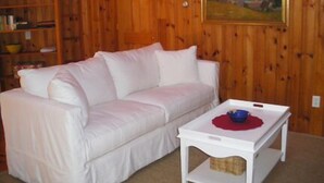 Ein weißes Sofa in einem Raum mit Holzvertäfelung, ein weißer Couchtisch mit einer roten Unterlage und ein Gemälde an der Wand.