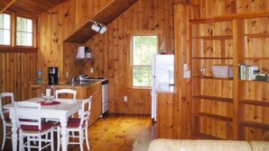Ein Holzblockhaus-Interieur mit Esstisch, Stühlen, einer Küchenzeile und einem Bücherregal.