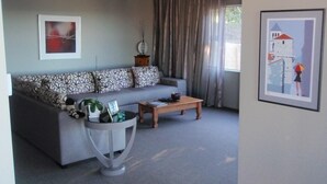 A living room with a grey sofa, a coffee table, a side table with a plant, and a framed picture on the wall. - Luxury Rotorua Executive Home with Lake Views: Relax, Unwind, and Enjoy (Rotorua Township)