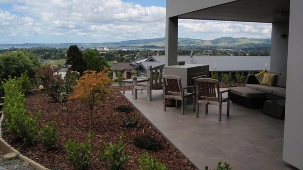 A modern outdoor patio with a view of distant hills and a cloudy sky. - Luxury Rotorua Executive Home with Lake Views: Relax, Unwind, and Enjoy (Rotorua Township)