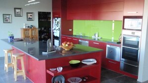 A modern kitchen with red cabinetry, a central island with stools, and stainless steel appliances. - Luxury Rotorua Executive Home with Lake Views: Relax, Unwind, and Enjoy (Rotorua Township)