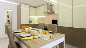 A modern dining area with a wooden table set for four, equipped with plates, cutlery, and a bowl of oranges. - Cosy duplex in Alfama (Lisboa)