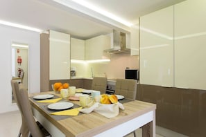 Un espace repas moderne avec une table en bois dressée pour quatre personnes, agrémentée d’assiettes, de couverts et d’un saladier rempli d’oranges.