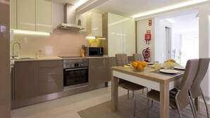 A modern kitchen with stainless steel appliances, a dining area with a table set for two, and a visible fire extinguisher on the wall. - Cosy duplex in Alfama (Lisboa)