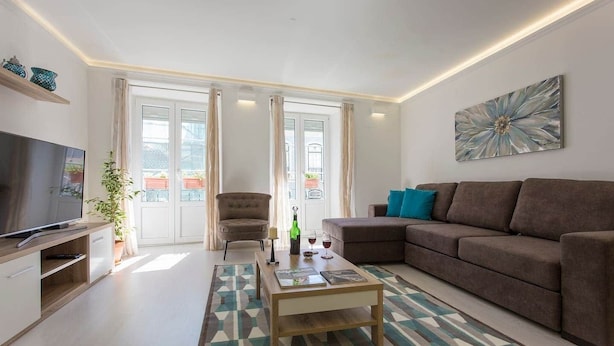 A modern living room with a flat-screen TV, a sofa, a chair, and a coffee table. - Cosy duplex in Alfama (Lisboa)