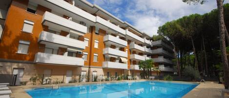 Un edificio residencial de varios pisos con balcones, una piscina y un jardín ajardinado.