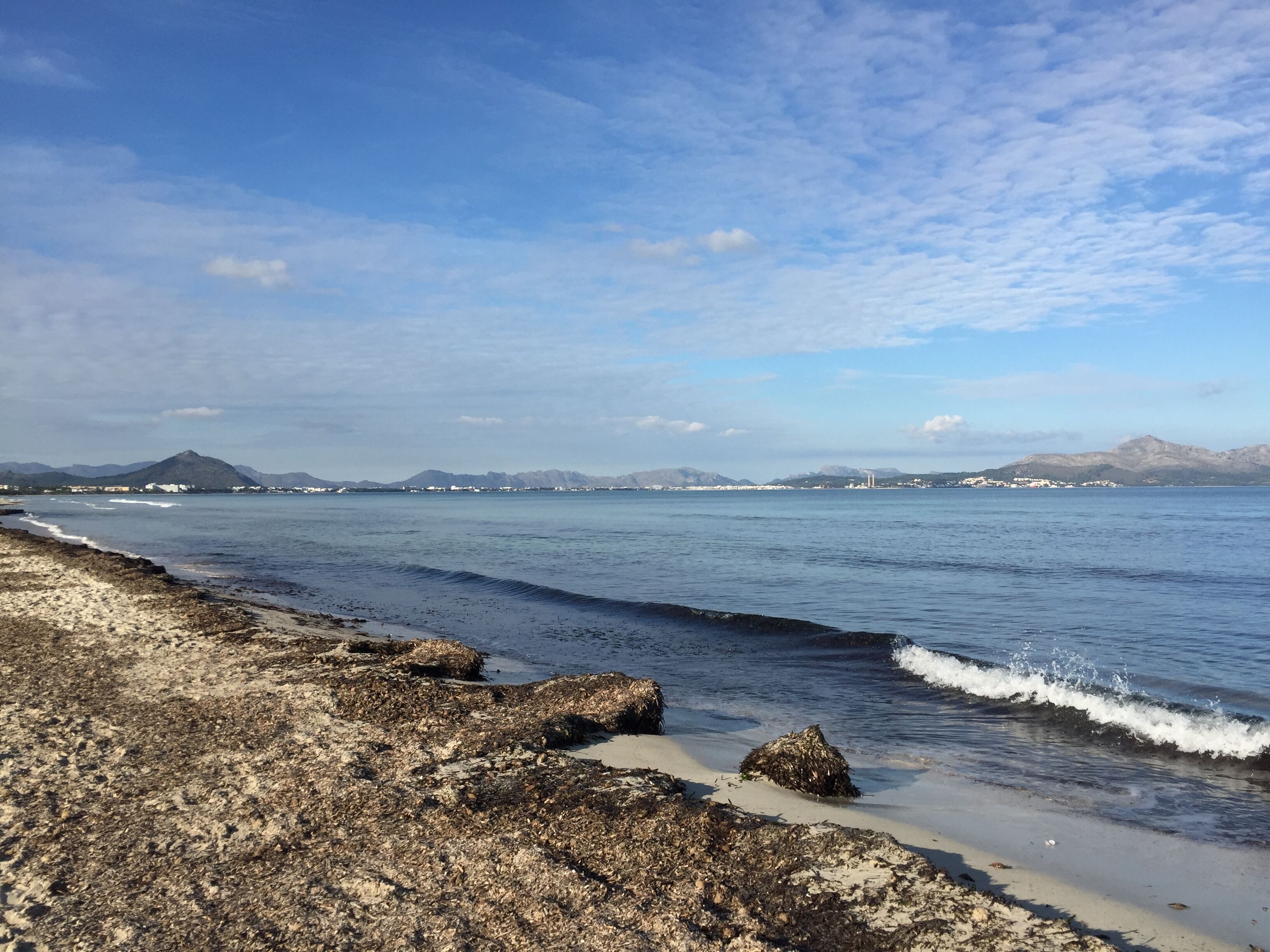 A coastal landscape with rocky shoreline, calm sea, and distant mountains.