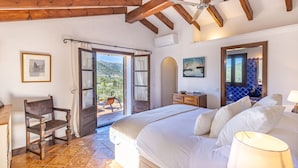 A bedroom with a large bed, a wooden chair, a desk, and a view of the outdoors. - Luxury secluded Villa with Infinity Pool &Panoramic view 20 minutes from beaches (Campanet)