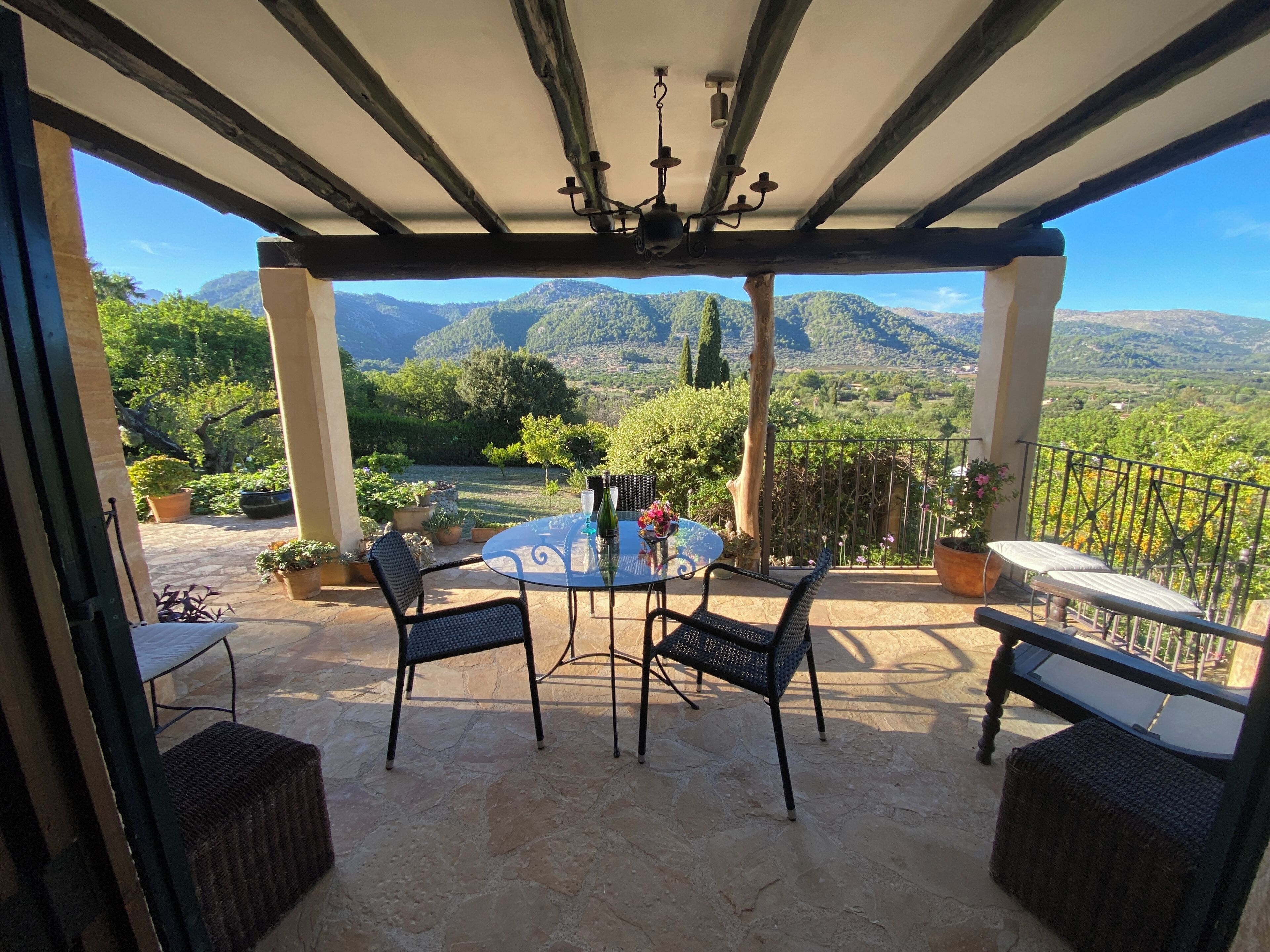 A covered patio with a table and chairs, potted plants, and a view of mountains.