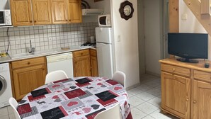 A compact kitchen with wooden cabinets, a microwave, a refrigerator, and a dining table with a quilted tablecloth. - Chalet - CHANTEMERLE (Saint-Chaffrey)