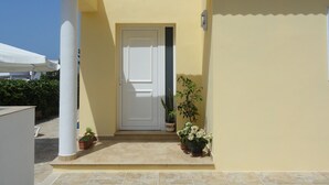A yellow building with a white door, potted plants, and a tiled entrance area.