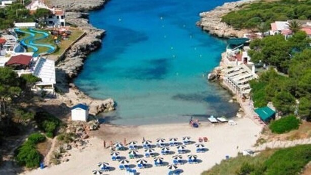 A coastal resort with a beach, a swimming pool, and a rocky shoreline.