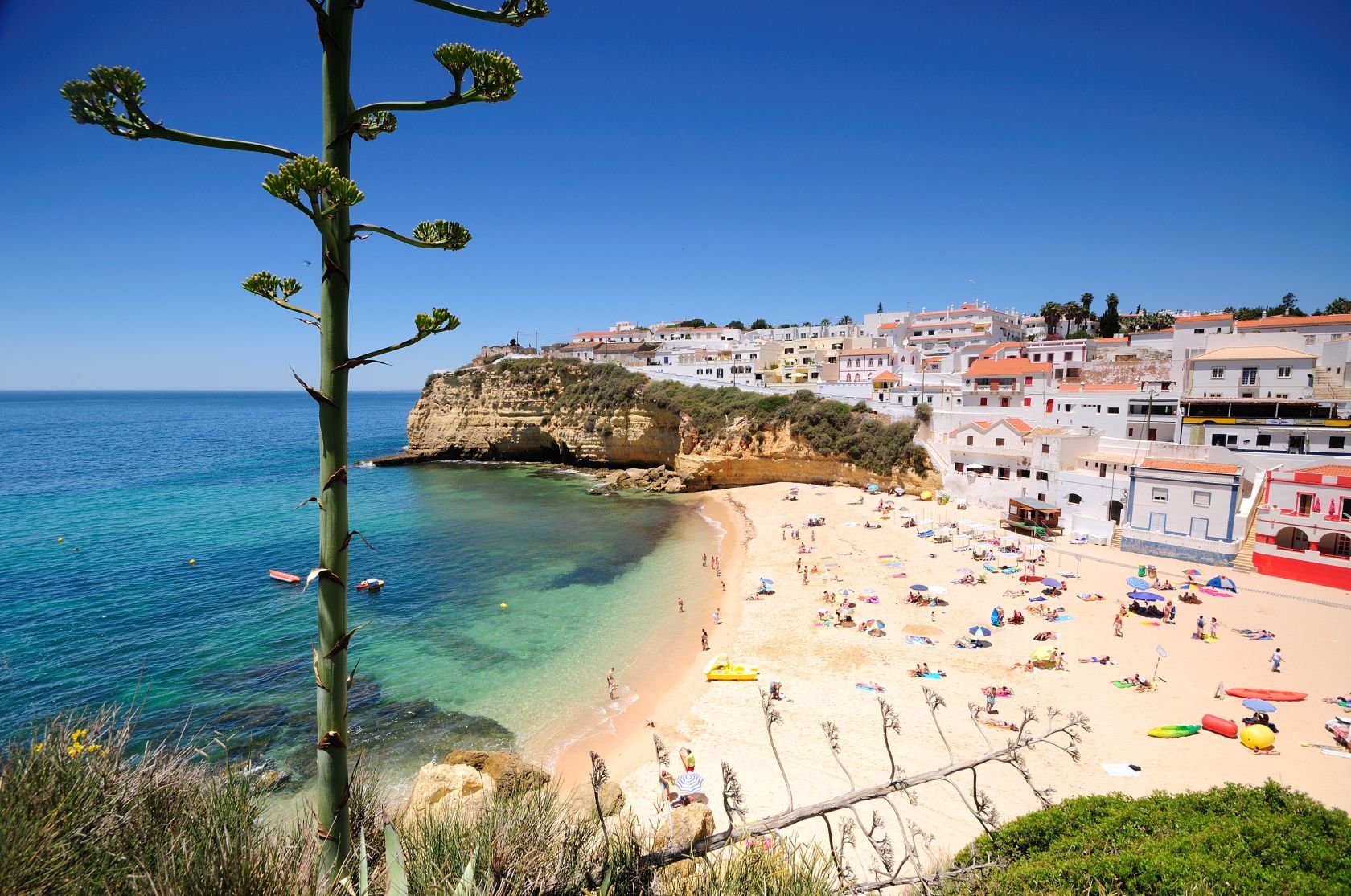 A coastal town with a beach, clear blue sea, and buildings along the cliff.