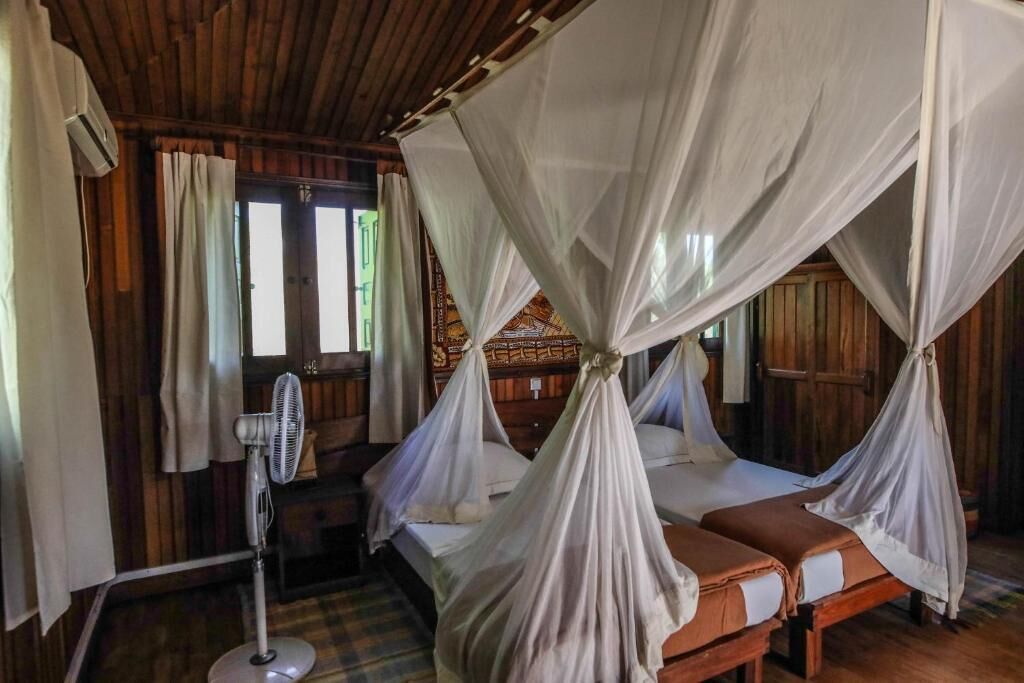 A room with two beds, each with a canopy, a standing fan, and wooden walls.