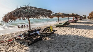Ein Strand mit Strohdächern, Liegestühlen und Menschen im Wasser.