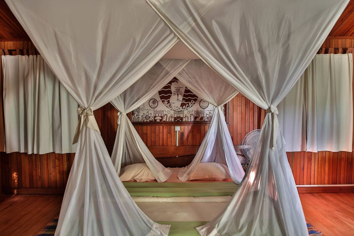 Una cama con dosel, paredes de madera y un ventilador.
