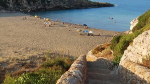 A beach with a stone staircase leading down to the water, surrounded by rocky cliffs and greenery.