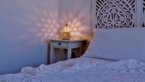 A neatly made bed with a white lace bedspread, a bedside table with a lamp, and a decorative wall panel.