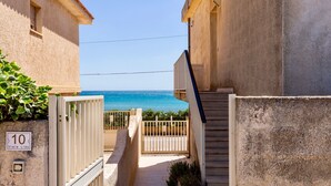 A narrow pathway leading to a gated entrance with a view of the sea.