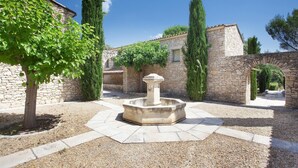 A courtyard with a central fountain, stone walls, and a tree. - Maisonette in Gordes with Provençal Charm (GORDES)