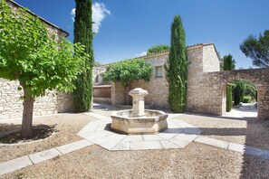 A courtyard with a central fountain, stone walls, and a tree. - Maisonette in Gordes with Provençal Charm (GORDES)