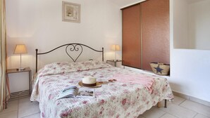 A neatly made bed with floral bedding, two bedside lamps, a star-patterned basket, and a framed picture on the wall. - Maisonette in Gordes with Provençal Charm (GORDES)