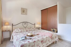 A neatly made bed with floral bedding, two bedside lamps, a star-patterned basket, and a framed picture on the wall. - Maisonette in Gordes with Provençal Charm (GORDES)