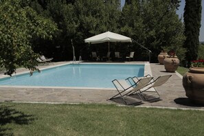 Une piscine rectangulaire avec un parasol blanc, entourée de dalles de pierre et de gazon.