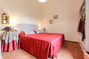 Une chambre à coucher avec une couvre-lit rouge, deux tables de chevet avec des lampes, un chemin de table à motifs floraux et un miroir au mur.