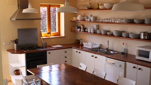 Una cocina con una mesa de madera, armarios blancos, una estufa y estantes con vajilla y vasos.