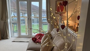 Una sala de estar acogedora con un sofá, un árbol decorativo con luces y vistas a través de un ventanal.