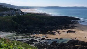 Vista costera con playa, costa rocosa y edificios al fondo.