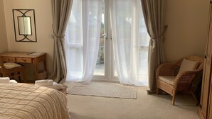 Un dormitorio con cama, una silla, un escritorio y una ventana con cortinas.