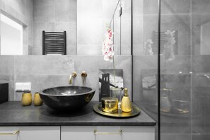 Un baño moderno con un lavamanos negro grande, accesorios dorados y un florero con flores.
