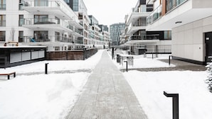 Un sendero cubierto de nieve entre edificios de apartamentos modernos con balcones y ventanas amplias.
