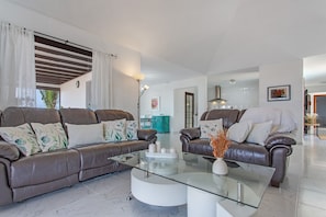 A modern living room with two leather sofas, a glass coffee table, and a teal cabinet in the background.