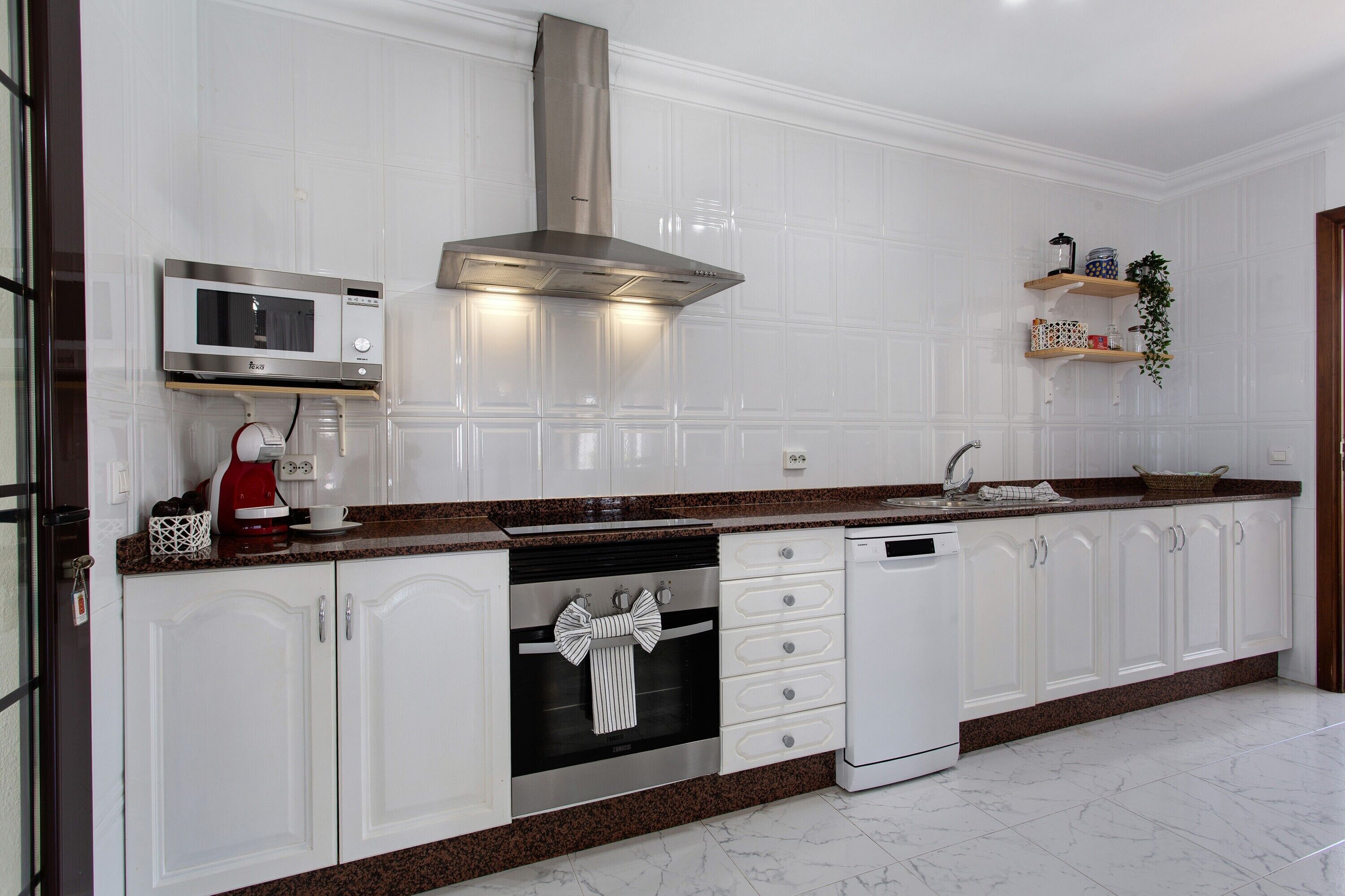 A modern kitchen with white cabinetry, a stainless steel range hood, a microwave, and a dishwasher.