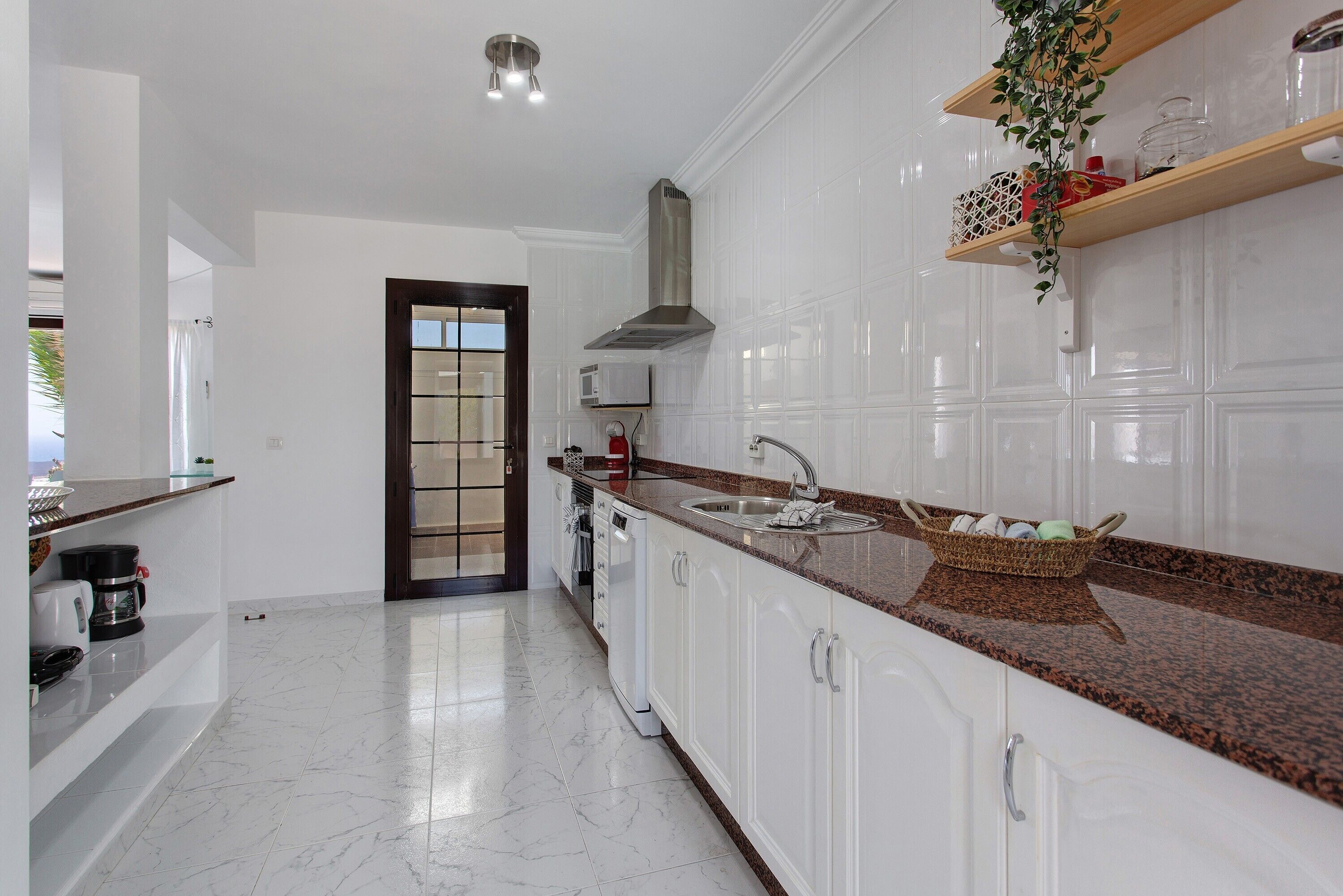 A modern kitchen with white cabinets, a granite countertop, a stainless steel range hood, and a built-in microwave.